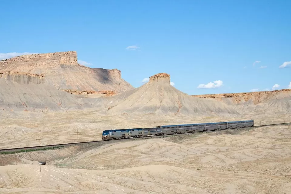 An Amtrak train passing through desert landscape with mesas in Utah.